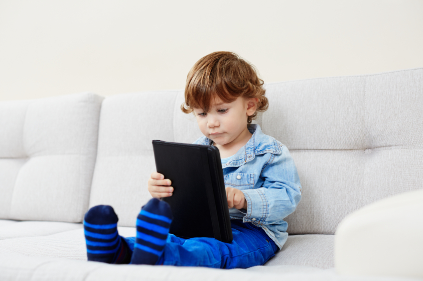 a young boy sitting on a sofa with a tablet