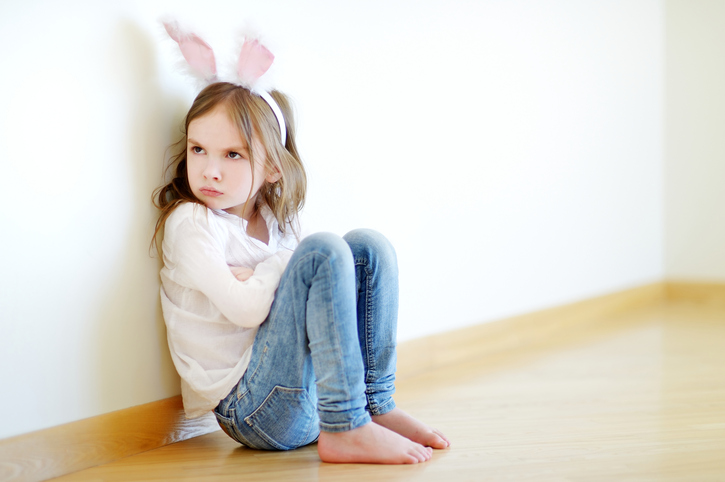 Very angry little girl wearing bunny ears sitting on a floor at home